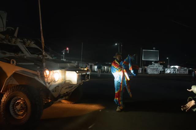 TOPSHOT - A Congolese supporter dressed in the colors of the Democratic Republic of Congo's national flag stands in front of an armoured personnel carrier (APC) as he celebrates the Leopards' equalizing goal in a street in Bunia at night during a FIFA World Cup match between DR Congo and Portugal in Bunia, Ituri Province, Democratic Republic of Congo, on June 17, 2026. The Congolese Leopards played their first match of the tournament in Houston, Texas (United States), against Portugal (1–1). The Democratic Republic of Congo (DRC) had last qualified for a World Cup in 1974. The country was then called Zaire, and the dictator Mobutu Sese Seko was in power (1965–1997). At nightfall in downtown Bunia, the capital of Ituri (northeast), a crowd gathered in the street, standing in front of a modest television screen. Above a barbecue where skewers sold individually were grilling, the owner of a small stall had hung up a screen so people could watch the match. (Photo by Jospin Mwisha / AFP)