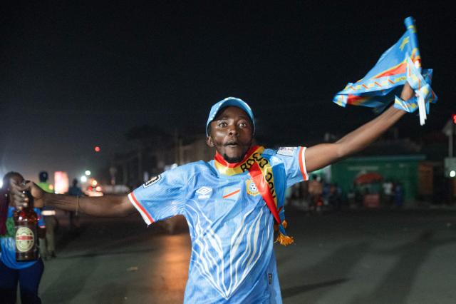 Congolese supporters dressed in the colors of the Democratic Republic of Congo's national flag celebrate the Leopards' equalizing goal in a street in Bunia at night during a FIFA World Cup match between DR Congo and Portugal in Bunia, Ituri Province, Democratic Republic of Congo, on June 17, 2026. The Congolese Leopards played their first match of the tournament in Houston, Texas (United States), against Portugal (1–1). The Democratic Republic of Congo (DRC) had last qualified for a World Cup in 1974. The country was then called Zaire, and the dictator Mobutu Sese Seko was in power (1965–1997). At nightfall in downtown Bunia, the capital of Ituri (northeast), a crowd gathered in the street, standing in front of a modest television screen. Above a barbecue where skewers sold individually were grilling, the owner of a small stall had hung up a screen so people could watch the match. (Photo by Jospin Mwisha / AFP)