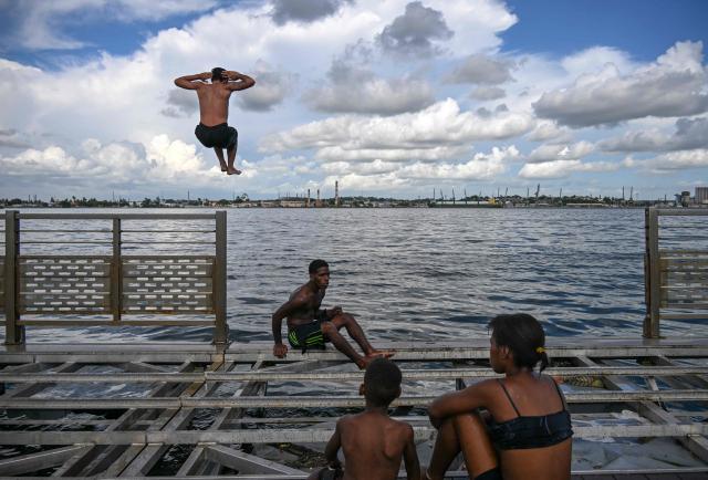 Young people jump into the water from a partially dismantled floating dock in Havana Bay on June 17, 2026. (Photo by YAMIL LAGE / AFP)