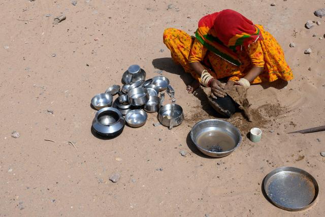 This photograph taken on May 29, 2026 shows herdsman Sawai Singh Bhati's wife, Seema Kawar washing utensils with mud to save water in 42 degrees Celsius temperatures, outside her house in Sanwata village on the outskirts of Rajasthan's Jaisalmer city. In India's hot plains, scorching summers have become increasingly harder to endure, requiring adaptations and forcing life into the hours of dark before the sun turns punishing. Temperatures in Singh's Sanwata village hit 45C in early June, as is often during the summer with the highest temperature recorded in the area as 49C. (Photo by Manan VATSYAYANA / AFP)