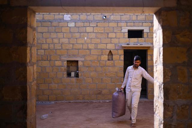 This photograph taken on May 29, 2026 shows herdsman Sawai Singh Bhati carrying cattle feed from inside his house in Sanwata village on the outskirts of Rajasthan's Jaisalmer city. In India's hot plains, scorching summers have become increasingly harder to endure, requiring adaptations and forcing life into the hours of dark before the sun turns punishing. Temperatures in Singh's Sanwata village hit 45C in early June, as is often during the summer with the highest temperature recorded in the area as 49C. (Photo by Manan VATSYAYANA / AFP)