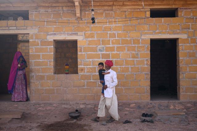 This photograph taken on May 29, 2026 shows herdsman Sawai Singh Bhati's father, Khet Singh carrying his grandson at their house in Sanwata village on the outskirts of Rajasthan's Jaisalmer city. In India's hot plains, scorching summers have become increasingly harder to endure, requiring adaptations and forcing life into the hours of dark before the sun turns punishing. Temperatures in Singh's Sanwata village hit 45C in early June, as is often during the summer with the highest temperature recorded in the area as 49C. (Photo by Manan VATSYAYANA / AFP)