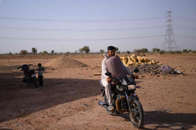 This photograph taken on May 29, 2026 shows herdsman Sawai Singh Bhati carrying cattle feed on his motorcycle in 40 degrees Celsius temperatures, outside his house in Sanwata village on the outskirts of Rajasthan's Jaisalmer city. In India's hot plains, scorching summers have become increasingly harder to endure, requiring adaptations and forcing life into the hours of dark before the sun turns punishing. Temperatures in Singh's Sanwata village hit 45C in early June, as is often during the summer with the highest temperature recorded in the area as 49C. (Photo by Manan VATSYAYANA / AFP)