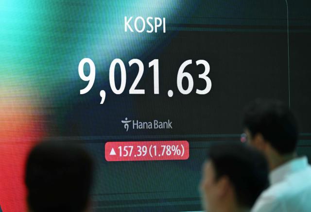 Currency dealers stand in front of a screen showing South Korea's benchmark stock index (KOSPI) as it breaks 9,000 points in a foreign exchange dealing room at the Hana Bank headquarters in Seoul on June 18, 2026. South Korea's benchmark Kospi index topped 9,000 points for the first time on June 18, on the back of a tech-fuelled rally led by chip titans Samsung and SK hynix. (Photo by Jung Yeon-je / AFP)
