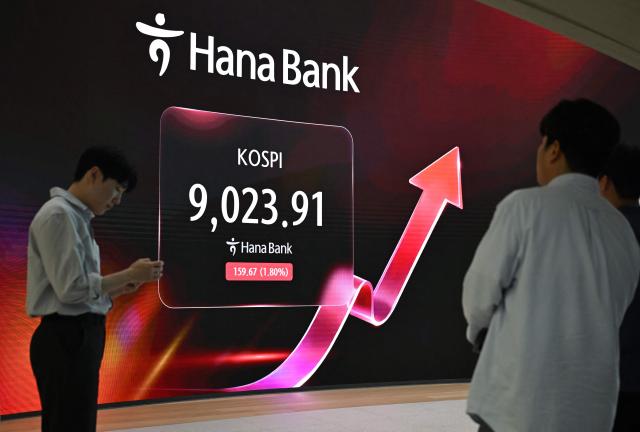 Currency dealers stand in front of a screen showing South Korea's benchmark stock index (KOSPI) as it breaks 9,000 points in a foreign exchange dealing room at the Hana Bank headquarters in Seoul on June 18, 2026. South Korea's benchmark Kospi index topped 9,000 points for the first time on June 18, on the back of a tech-fuelled rally led by chip titans Samsung and SK hynix. (Photo by Jung Yeon-je / AFP)