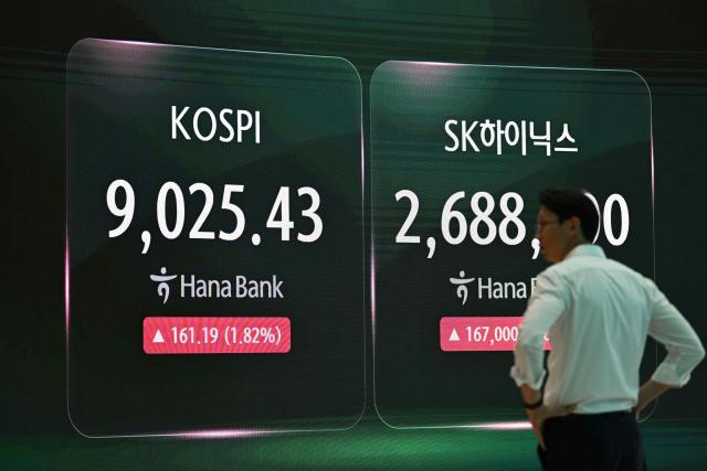 A currency dealer stands in front of a screen showing South Korea's benchmark stock index (KOSPI) as it breaks 9,000 points in a foreign exchange dealing room at the Hana Bank headquarters in Seoul on June 18, 2026. South Korea's benchmark Kospi index topped 9,000 points for the first time on June 18, on the back of a tech-fuelled rally led by chip titans Samsung and SK hynix. (Photo by Jung Yeon-je / AFP)