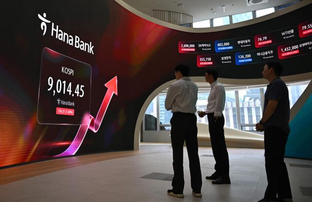 Currency dealers stand in front of a screen showing South Korea's benchmark stock index (KOSPI) as it breaks 9,000 points in a foreign exchange dealing room at the Hana Bank headquarters in Seoul on June 18, 2026. South Korea's benchmark Kospi index topped 9,000 points for the first time on June 18, on the back of a tech-fuelled rally led by chip titans Samsung and SK hynix. (Photo by Jung Yeon-je / AFP)