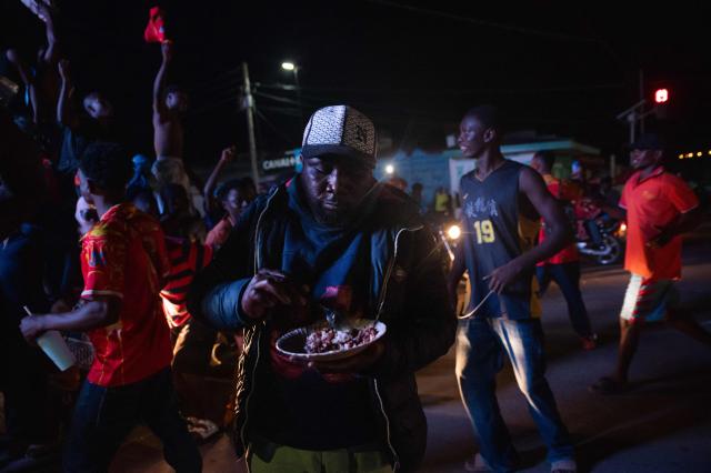 A man eats a plate of food as Congolese supporters celebrate the Leopards' equalizing goal in a street in Bunia at night during a FIFA World Cup match between DR Congo and Portugal in Bunia, Ituri Province, Democratic Republic of Congo, on June 17, 2026. Ituri, a remote province in northeastern Congo, is at the epicenter of the 17th Ebola outbreak, declared on May 15 in the DRC. The virus has infected 837 people and caused 196 deaths so far, according to the latest official figures.
In the city of Bunia alone, 215 cases of infection have been confirmed, while the DRCs testing capacity is limited. The scale of the health crisis is still unknown, scientists, aid workers, and international health authorities acknowledge.
But for 90 minutes of the match, some of the roughly 100 million inhabitants say they were able to escape the worries linked to the epidemic, the conflict in the east of the country, and the violence of armed groups. (Photo by Jospin Mwisha / AFP)