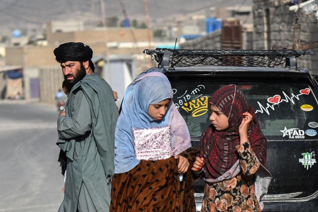 An Afghan man looks on as girls walk towards a madrassa or Islamic school in Kandahar on June 18, 2026. (Photo by Sanaullah SEIAM / AFP)