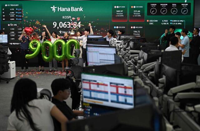 Currency dealers celebrate in front of a screen showing South Korea's benchmark stock index (KOSPI) during a ceremony celebrating it breaking 9,000 points in a foreign exchange dealing room at the Hana Bank headquarters in Seoul on June 18, 2026. South Korea's benchmark Kospi index topped 9,000 points for the first time on June 18, on the back of a tech-fuelled rally led by chip titans Samsung and SK hynix. (Photo by Jung Yeon-je / AFP)