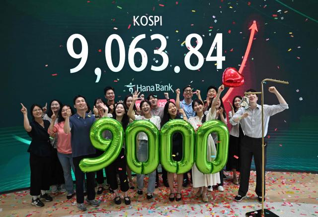 Currency dealers celebrate in front of a screen showing South Korea's benchmark stock index (KOSPI) during a ceremony celebrating it breaking 9,000 points in a foreign exchange dealing room at the Hana Bank headquarters in Seoul on June 18, 2026. South Korea's benchmark Kospi index topped 9,000 points for the first time on June 18, on the back of a tech-fuelled rally led by chip titans Samsung and SK hynix. (Photo by Jung Yeon-je / AFP)
