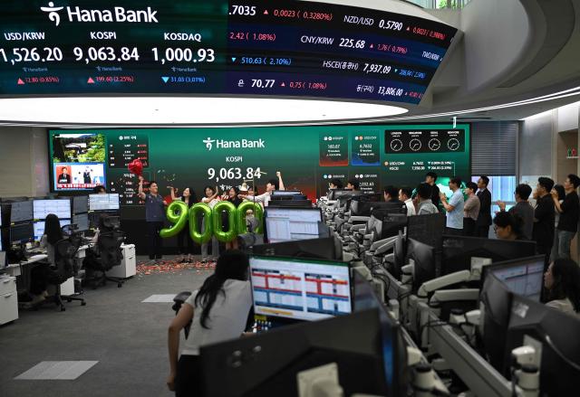Currency dealers celebrate in front of a screen showing South Korea's benchmark stock index (KOSPI) during a ceremony celebrating it breaking 9,000 points in a foreign exchange dealing room at the Hana Bank headquarters in Seoul on June 18, 2026. South Korea's benchmark Kospi index topped 9,000 points for the first time on June 18, on the back of a tech-fuelled rally led by chip titans Samsung and SK hynix. (Photo by Jung Yeon-je / AFP)