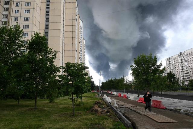 A woman walks in a residential locality as black smoke rises from the area of the Russian oil producer Gazprom Neft's Moscow oil refinery on the south-eastern outskirts of Moscow on June 18, 2026. Moscow was fending off a "large-scale" drone attack from Ukraine, with several drones reaching an oil refinery, the city's mayor Sergey Sobyanin said early on June 18, 2026. (Photo by AFP)