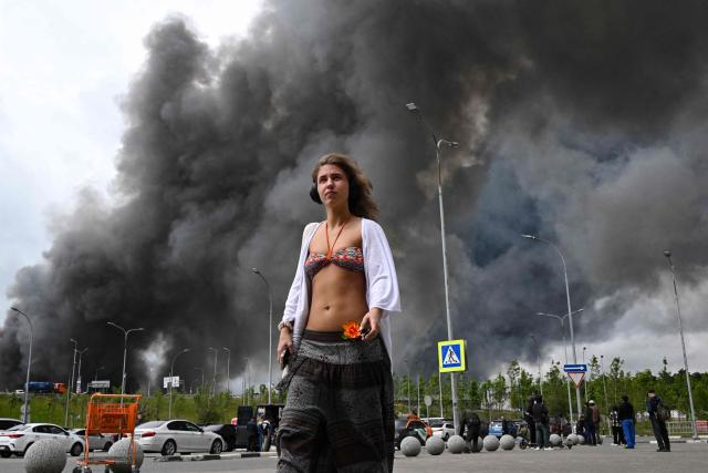 TOPSHOT - A woman walks outside a shopping mall as black smoke rises from the area of the Russian oil producer Gazprom Neft's Moscow oil refinery on the south-eastern outskirts of Moscow on June 18, 2026. Moscow was fending off a "large-scale" drone attack from Ukraine, with several drones reaching an oil refinery, the city's mayor Sergey Sobyanin said early on June 18, 2026. (Photo by AFP)