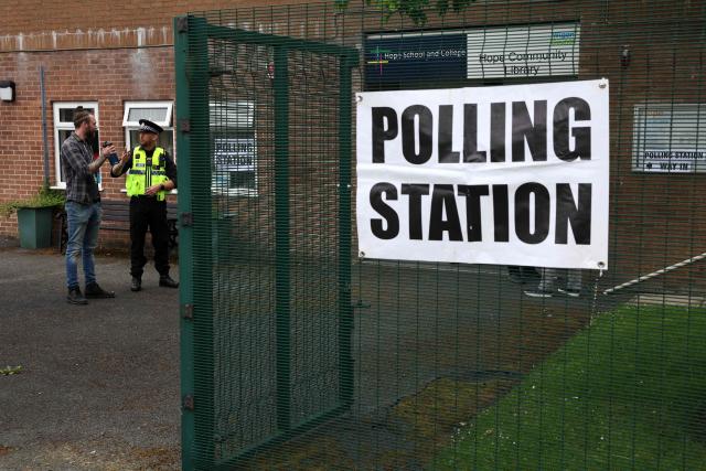 A police officer stands on duty as people arrive to cast their vote  in the the Makerfield by-election, at a polling station set up at a Library in Winstanley, part of the Makerfield parliamentary constituency, in north west England on June 18, 2026. Britain holds a unique vote on June 18 that could trigger the endgame for Labour leader Keir Starmer's beleaguered premiership, or win him a reprieve. (Photo by Darren Staples / AFP)