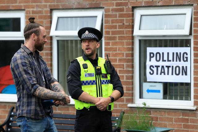 A police officer stands on duty as people arrive to cast their vote  in the the Makerfield by-election, at a polling station set up at a Library in Winstanley, part of the Makerfield parliamentary constituency, in north west England on June 18, 2026. Britain holds a unique vote on June 18 that could trigger the endgame for Labour leader Keir Starmer's beleaguered premiership, or win him a reprieve. (Photo by Darren Staples / AFP)