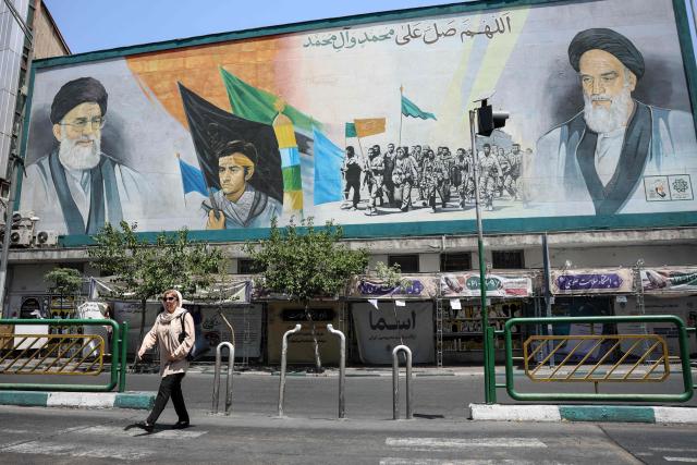 An Iranian woman walks past a mural depicting late Iranian supreme leaders Ayatollah Ali Khamenei (L) and Ayatollah Ruhollah Khomeini (R) in Tehran on June 18, 2026. The United States and Iran have signed a deal to end the Middle East war, with a ceremony set for June 19 in Switzerland that will mark the start of a 60-day negotiation period. The memorandum of understanding aims to put an end to months of conflict initiated by US-Israeli strikes on Iran in February, which wreaked chaos across the region and rattled the global economy. (Photo by AFP) / 