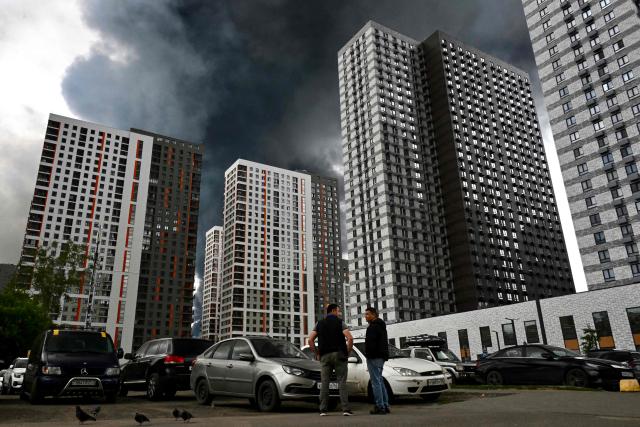 Men interact in a residential locality blanketed in black smoke in Moscow on June 18, 2026. Moscow was fending off a "large-scale" drone attack from Ukraine, with several drones reaching an oil refinery, the city's mayor Sergey Sobyanin said early on June 18, 2026. (Photo by AFP)