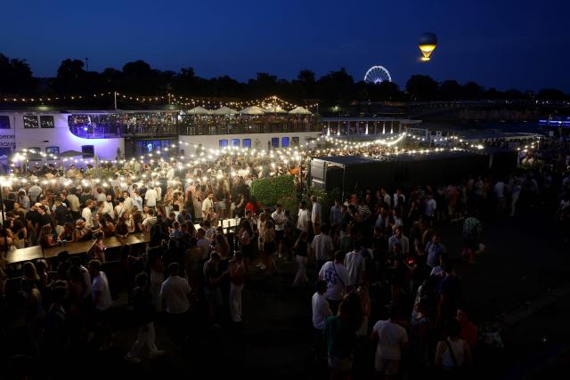 (FILES) People attend France's annual street music festival, the Fete de la Musique, on the Seine river banks as the Paris 2024 Olympic cauldron tethered to a balloon flies above the Tuileries garden at sunset in Paris on June 21, 2025. Like every year the French midsummer Festival of Music also known as Fete de la Musique is set to take place in France, on the day of summer solstice June 21. (Photo by ROMAIN PERROCHEAU / AFP)