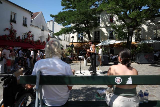 (FILES) Music enthusiasts listen to singer Nick Mallen perfomring in Montmartre during the French midsummer Festival of Music (Fete de la Musique) in Paris on June 21, 2025. Like every year the French midsummer Festival of Music also known as Fete de la Musique is set to take place in France, on the day of summer solstice June 21. (Photo by ROMAIN PERROCHEAU / AFP)