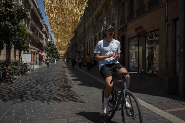 A cyclist rides along a street covered by an installation to provide shade from the sun, in Toulouse on June 18, 2026. (Photo by Ed JONES / AFP)