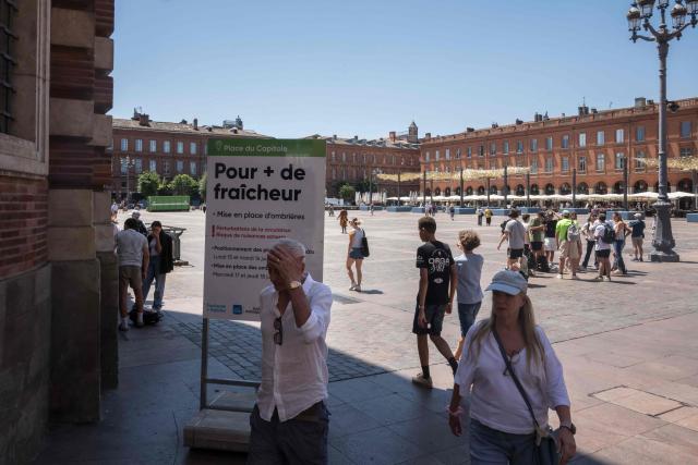 Pedestrians walk past a sign advising about an upcoming installation to provide shelter from the sun, at the central Capitol square in Toulouse on June 18, 2026. (Photo by Ed JONES / AFP)