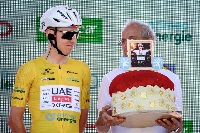 UAE Team Emirates XRG’s Slovenian rider Tadej Pogacar (L) looks on as he receives a 5kg pudding from a baker during the team presentation of the second stage of the Men’s Tour of Switzerland (Tour de Suisse) cycling race in Locarno, Switzerland, on June 18, 2026. (Photo by Fabrice COFFRINI / AFP)