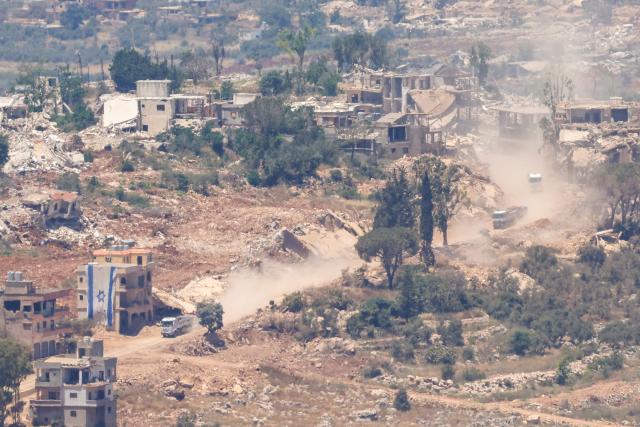 This picture taken from a position in the Upper Galilee in northern Israel, shows an Israeli construction truck passing an Israeli flag covering part of a destroyed building in the southern Lebanese village of Taybeh near the border on June 18, 2026. Israeli strikes in south Lebanon killed three people on June 18, according to Lebanese state media, hours after the United States and Iran signed an agreement to end the Middle East war. Israel's military, meanwhile, announced the death of one of its soldiers the night before in an incident in south Lebanon that also left seven others wounded. (Photo by Jalaa MAREY / AFP)