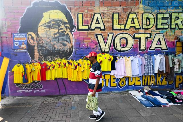 A man walks past Colombia's national football team jerseys for sale and a mural of presidential canditate Ivan Cepeda, of the Pacto Historico party, for the upcoming presidential election in Cali, Colombia, on June 18, 2026. Colombians vote on June 21, 2026 in a presidential runoff pitting a hard-right opera-singer-turned-lawyer against a leftist senator, an election with stark consequences for the country's stumbling peace process with armed groups and strained ties with Washington. (Photo by JOAQUIN SARMIENTO / AFP)