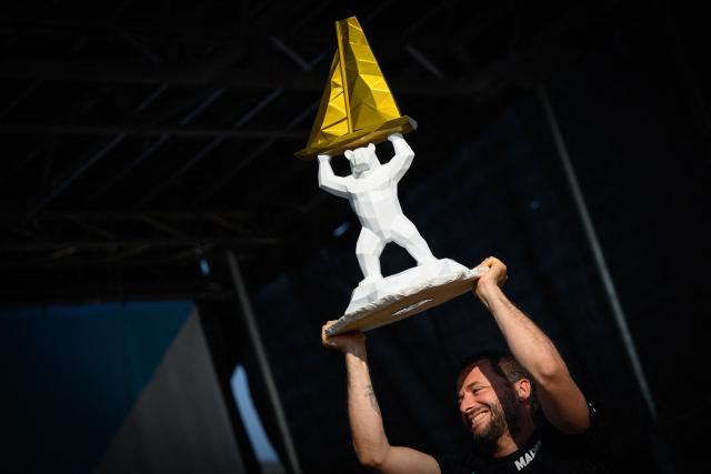 "Allagrande Mapei" Imoca monohull Italian skipper Ambrogio Beccaria celebrates whith his trophy on the podium after winning the Vendee Arctique solo sailing race, in Les Sables-d'Olonne on June 18, 2026. Beccaria won the Vendee Arctique the night of June 15, the first qualifying race for the 2028 Vendee Globe, with a close finish marked by a tribute to French offshore sailor and Vendee Globe 2024/2025 winner Charlie Dalin, who died in Quimper, western France, aged 42, from cancer, his family announced on June 11, 2026. (Photo by Loic VENANCE / AFP)