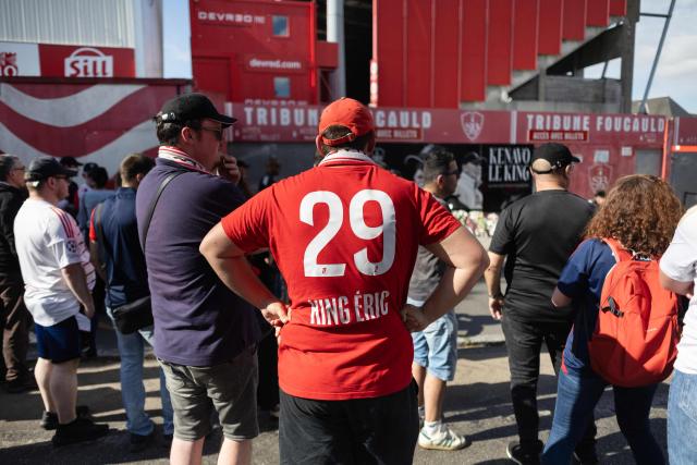 An attendee wearing a Stade Brestois football jersey bearing de department number for Finistere "29" and the name of the late Stade Brestois team's head coach Eric Roy looks on at the entrance of the Francis-Le Ble stadium in Brest, western France on June 18, 2026 to pay tribute to the late Stade Brestois coach Eric Roy who died on day prior. Brest coach Eric Roy, 58, has died from pancreatic cancer on June 17, his family announced on via the late manager’s Instagram account. (Photo by Fred TANNEAU / AFP)
