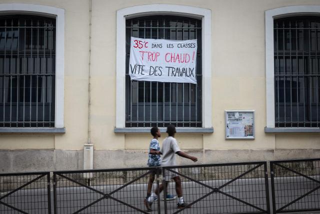 Children walk past a banner which reads "35 degrees in the classrooms, too hot. Work needs to be done quickly" on a window of a school in Paris on June 18, 2026. (Photo by Simon WOHLFAHRT / AFP)