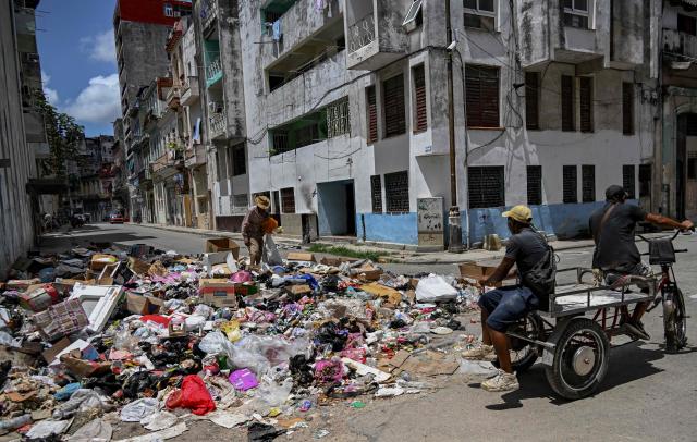 People ride past discarded garbage as a man rummages through it on a street in Havana on June 18, 2026. (Photo by YAMIL LAGE / AFP)