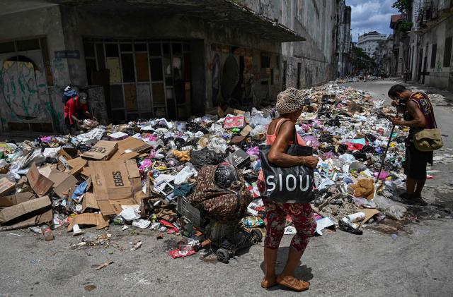 A woman walks past discarded garbage as other people rummage through it on a street in Havana on June 18, 2026. (Photo by YAMIL LAGE / AFP)