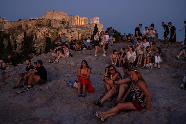 Tourists watch the sunset as they sit on Areopagus hill overlooking the ancient Acropolis, in Athens on June 18, 2026. Greece's culture ministry on June 18, 2026 said it had finished a lengthy restoration, after 220 years, of the western facade of the Parthenon in Athens, re-creating the world-famous monument's early 1800s look. The 2,500-year-old temple honouring the goddess Athena, which sits on a hill overlooking the Greek capital, is visited by more than four million people each year. (Photo by Angelos TZORTZINIS / AFP)