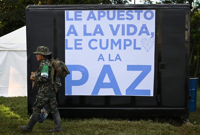 A member of the Coordinadora Nacional Ejercito Bolivariano (CNEB) guerrilla group carries a monkey in front of a banner reading "I Bet on Life, I Fulfill Peace" during a disarmament ceremony agreed with the Colombian government in Valle del Guamuez, Putumayo department, Colombia on June 18, 2026. Three days before a runoff vote set to determine the continuation of the country's first leftist government, this marks a first step for the rebels to settle in a special zone where they aim to consolidate agreements with the government. (Photo by Raul ARBOLEDA / AFP)