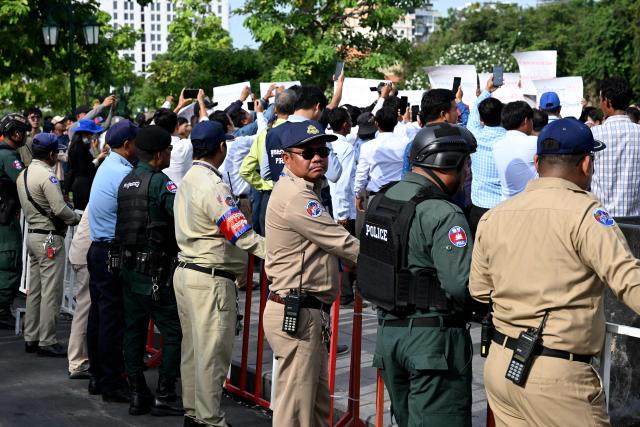 Police officials stand guard as supporters of Rong Chhun, an advisor of the Nation Power Party, hold placards outside the Supreme Court in Phnom Penh on June 19, 2026. Cambodia's top court on June 19 suspended a prison sentence handed to opposition politician Rong Chhun but upheld a ban on him running for office, his lawyer said, to the dismay of supporters. (Photo by TANG CHHIN Sothy / AFP)