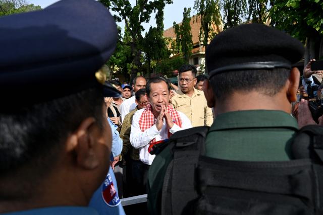 Rong Chhun (C), an advisor of the Nation Power Party, greets police officials outside the Supreme Court in Phnom Penh on June 19, 2026. Cambodia's top court on June 19 suspended a prison sentence handed to opposition politician Rong Chhun but upheld a ban on him running for office, his lawyer said, to the dismay of supporters. (Photo by TANG CHHIN Sothy / AFP)