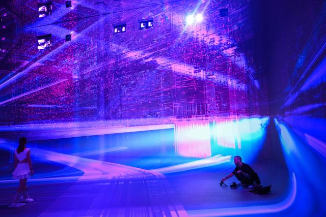 People take pictures while walking through immersive visualizations from the inaugural exhibition Machine Dreams: Rainforest are projected at DATALAND, the Museum of AI Arts, in Los Angeles, California on June 9, 2026. The squawks of macaws, the smell of wet earth after rain, and the swirl of colours will transport visitors to a Los Angeles museum to the heart of the Amazon rainforest -- or rather, an AI version of it. Data collected from those visitors  their movements, their heartbeats, and even the temperature of their skin -- will feed the computer that is creating the immersive display, using a network of sensors, including those on the wrists of ticket-holders. (Photo by Patrick T. Fallon / AFP)