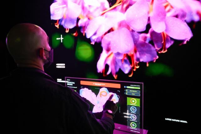 A guest touches a screen to interact with Immersive visualizations from the inaugural exhibition Machine Dreams: Rainforest are projected at DATALAND, the Museum of AI Arts, in Los Angeles, California on June 9, 2026. The squawks of macaws, the smell of wet earth after rain, and the swirl of colours will transport visitors to a Los Angeles museum to the heart of the Amazon rainforest -- or rather, an AI version of it. Data collected from those visitors  their movements, their heartbeats, and even the temperature of their skin -- will feed the computer that is creating the immersive display, using a network of sensors, including those on the wrists of ticket-holders. (Photo by Patrick T. Fallon / AFP)
