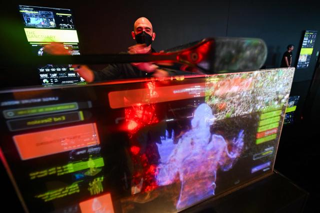 A guest gestures with a screen and cameras to interact with Immersive visualizations from the inaugural exhibition Machine Dreams: Rainforest are projected at DATALAND, the Museum of AI Arts, in Los Angeles, California on June 9, 2026. The squawks of macaws, the smell of wet earth after rain, and the swirl of colours will transport visitors to a Los Angeles museum to the heart of the Amazon rainforest -- or rather, an AI version of it. Data collected from those visitors  their movements, their heartbeats, and even the temperature of their skin -- will feed the computer that is creating the immersive display, using a network of sensors, including those on the wrists of ticket-holders. (Photo by Patrick T. Fallon / AFP)