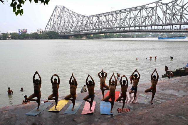 Traditional wrestlers practice yoga on the banks of the holy river Ganges with the backdrop of the iconic Howrah Bridge in Kolkata on June 19, 2026. (Photo by Dibyangshu SARKAR / AFP)