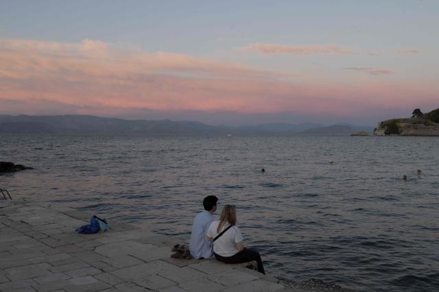 A couple sit by the Mediterranean sea, in the old town of Corfu at sunset, on the Greek island of Corfu on June 17, 2026. (Photo by Roman PILIPEY / AFP)