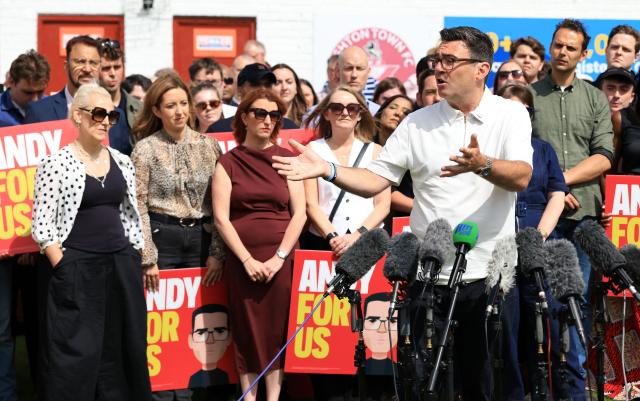 Marie-France van Heel (L), wife of new Labour Party MP for Makerfield, Andy Burnham, listens as her husband speaks to supporters and members of the media, the morning after his by-election victory, at Ashton Town FC, in Ashton in Makerfield, north-west England on June 19, 2026. Veteran UK Labour politician Andy Burnham emphatically won a crunch by-election on Friday, securing a parliamentary seat and clearing the way for a widely expected leadership challenge against beleaguered Prime Minister Keir Starmer. (Photo by Darren Staples / AFP)