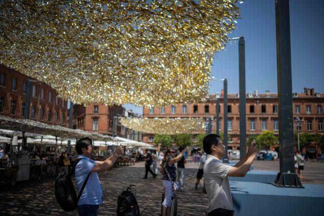 People take pictures on the Capitole square under a part covered by an installation to provide shade, in Toulouse on June 19, 2026. A heatwave hits France and is set to continue for several days with temperatures expected to reach up to 40°C in some areas on June 21, the first day of summer. (Photo by Lionel BONAVENTURE / AFP)