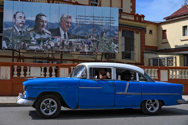 An old American car rides past a poster depicting Cuban late leader Fidel Castro (L), Cuba's former President Raul Castro (C) and Cuba's current President Miguel Diaz-Canel (R) in Havana, on June 19, 2026. Nearly 70 years after Fidel Castro's 1959 revolution, communist-run Cuba has adopted a sweeping package of free-market reforms aimed at extricating the country from a deep crisis. (Photo by YAMIL LAGE / AFP)
