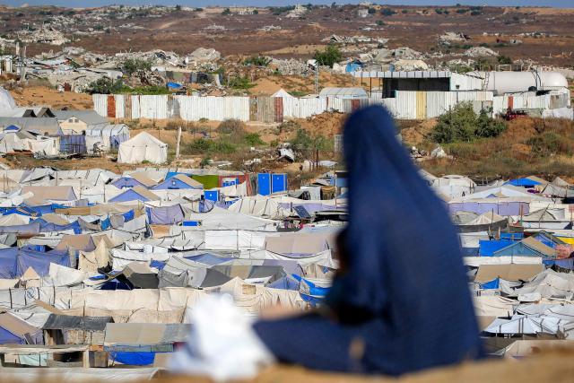 A woman sits along a promontory overlooking shelters for people displaced by war, at the Nuseirat camp for Palestinian refugees in the central Gaza Strip on June 19, 2026. Palestinian Islamist movement Hamas on Monday hailed a deal between the United States and Iran, expressing hope it would help put an end to violence in the Gaza Strip. Israel and Hamas trade near-daily accusations of truce violations and the Gaza Strip remains gripped by bloodshed as progress on permanently ending the war remains stalled. (Photo by Eyad Baba / AFP)