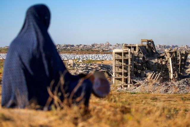 A woman sits along a promontory overlooking shelters for people displaced by war near a heavily-damaged buiilding at the Nuseirat camp for Palestinian refugees in the central Gaza Strip on June 19, 2026. Palestinian Islamist movement Hamas on Monday hailed a deal between the United States and Iran, expressing hope it would help put an end to violence in the Gaza Strip. Israel and Hamas trade near-daily accusations of truce violations and the Gaza Strip remains gripped by bloodshed as progress on permanently ending the war remains stalled. (Photo by Eyad Baba / AFP)