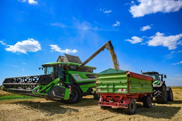 A combine harvester discharge wheat to a tractor trailer in a field near Manastirea village, southern Romania, on June 19, 2026. Romanian farmers have been forced to start the annual grain harvest weeks earlier than usual due to an intense early-summer heatwave and prolonged drought conditions driven by climate change, threatening crop yields across the region. (Photo by Daniel MIHAILESCU / AFP)