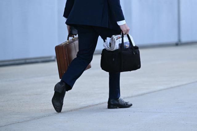 An aide to US President Donald Trump carries bags as he walks towards Air Force One at Joint Base Andrews in Maryland on June 19, 2026. Trump is heading to spend the weekend at the Camp David presidential retreat. (Photo by Brendan SMIALOWSKI / AFP)